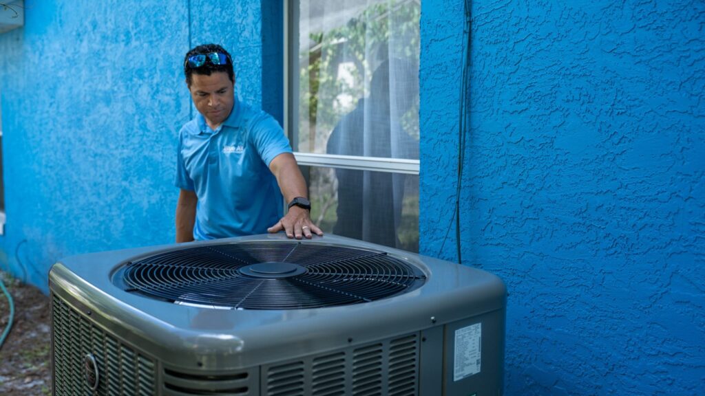 Blue Air technician with an outdoor AC unit against a blue wall